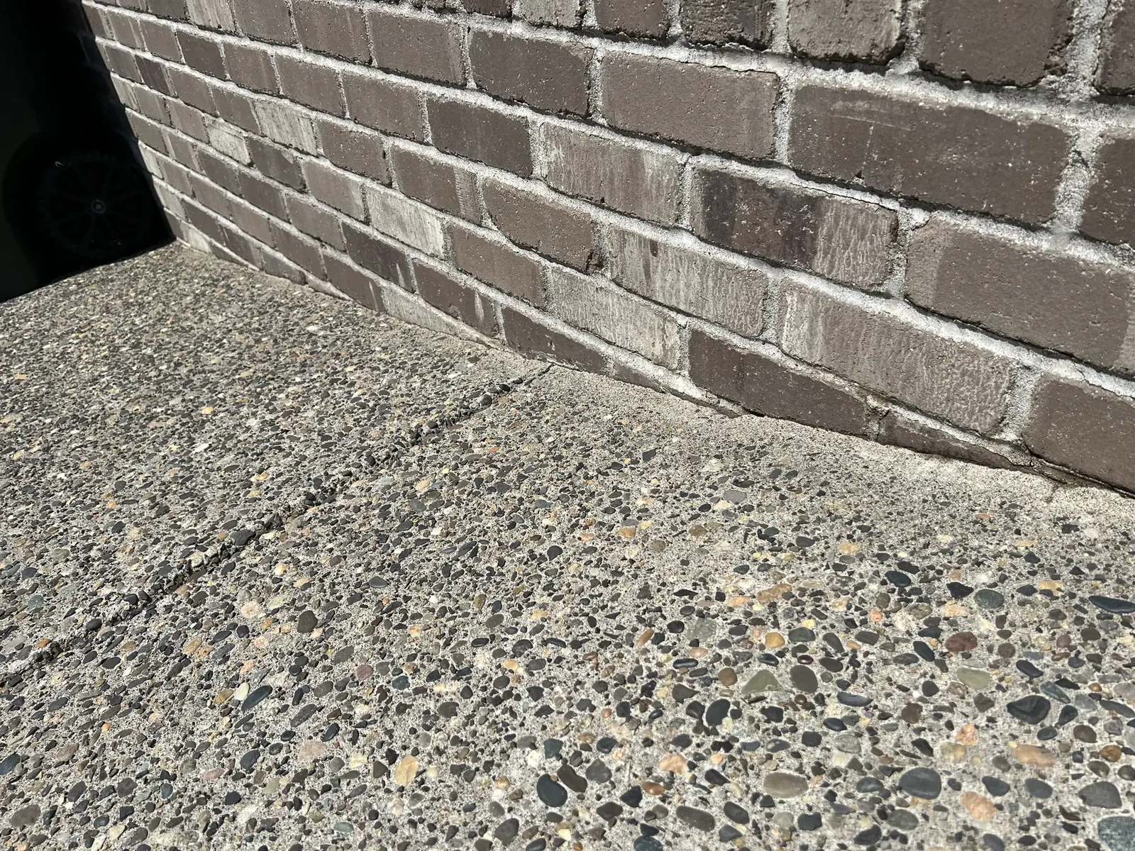 Clean driveway edge beside a brick wall after pressure washing
