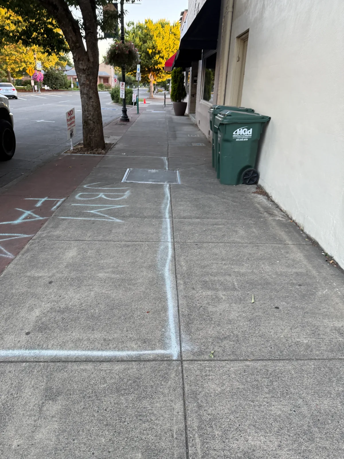 Large white parade chalk outlines on standard concrete sidewalk along NE 2nd Avenue before cleaning