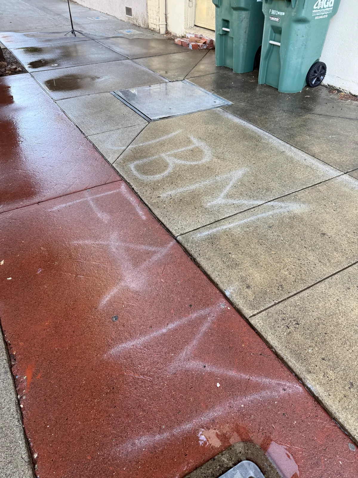 White parade chalk writing across gray and red sidewalk panels before cleaning in Downtown Hillsboro