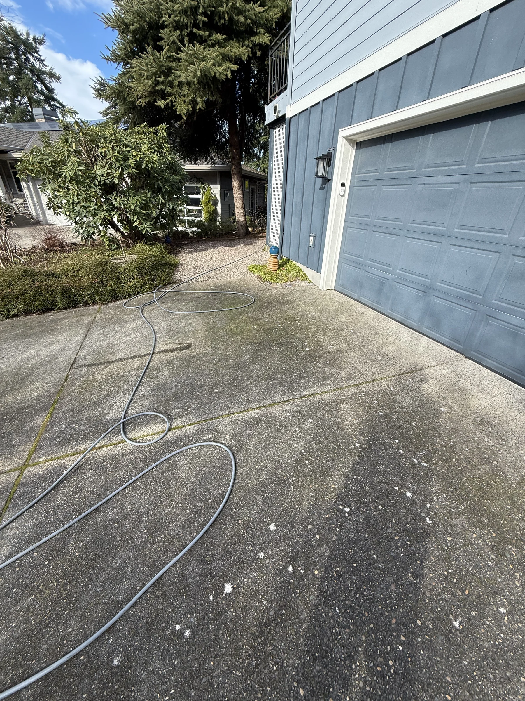 Concrete driveway beside a blue garage during a Rock Creek pressure washing project