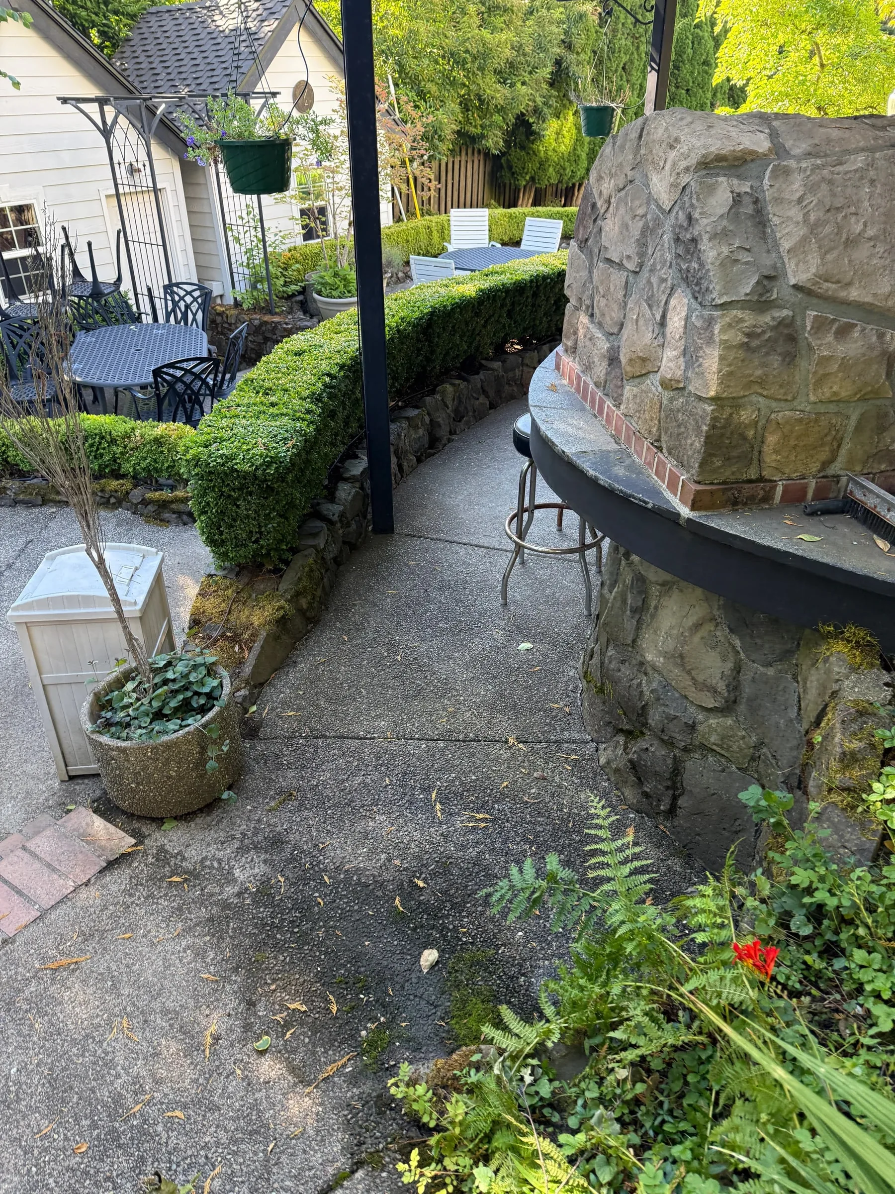 Shaded concrete walkway beside a stone outdoor kitchen before cleaning in West Beaverton